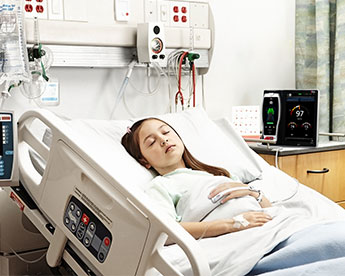 Patient in hospital bed wearing Masimo sensor with Root device in background.