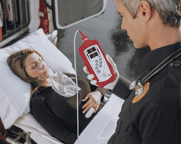 Emergency worker monitoring unconscious patient on gurney next to ambulance.