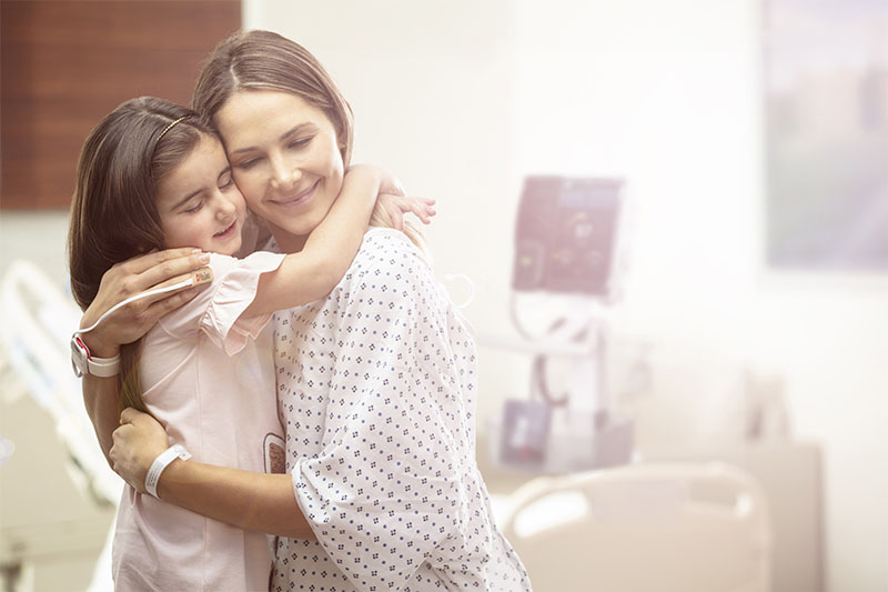 Patient in hospital wearing a hospital gown hugging child. 