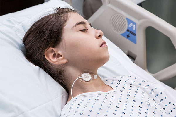 Child sleeping in hospital bed wearing neck sensor.