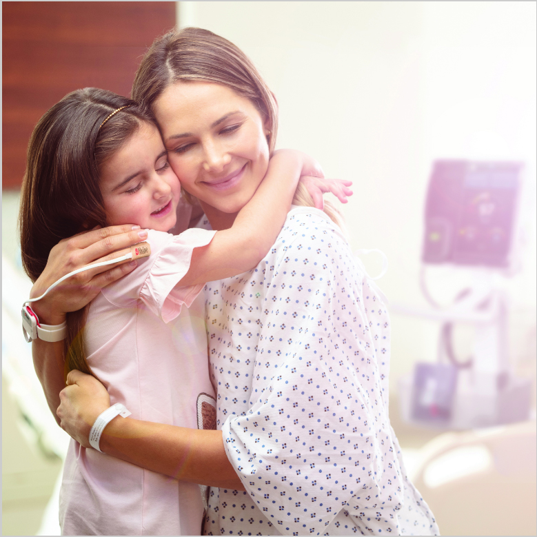 Adult patient wearing hospital gown wearing a Masimo sensor hugging a child.